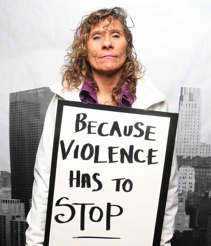 Person holding a sign reading "Because violence has to STOP"