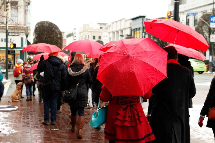 A line of people walking down a cobble street, all holding red umbrellas